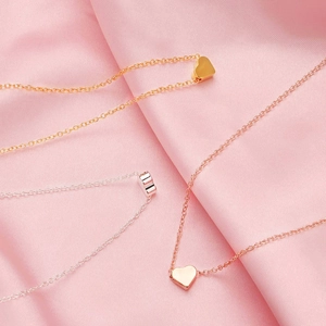 Detailed view of gold and silver heart pendant necklaces on pink satin fabric background