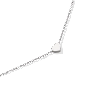 Macro detail of a minimalist silver heart pendant on a fine polished cable chain necklace