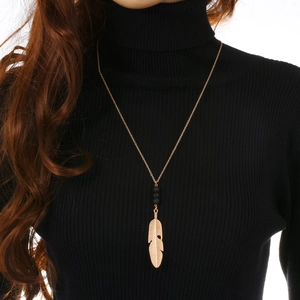 Detail of long gold feather pendant necklace with black beads on a black sweater background