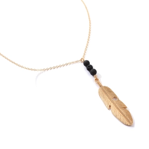 Macro detail of golden feather pendant with black lava beads and delicate cross chain