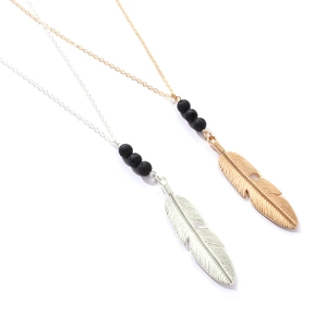 Detail view of gold and silver feather pendants with matte black lava stone beads