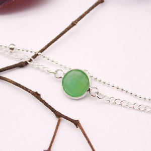 Macro detail of silver double-layer bracelet featuring a faceted green gemstone charm