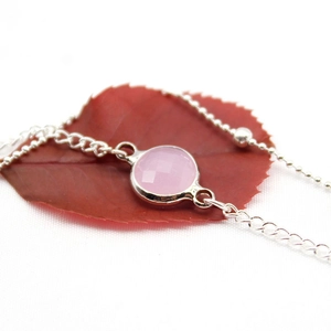 Macro detail of a silver-toned anklet featuring a round pink faceted gemstone charm