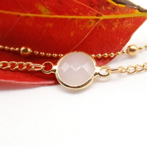 Macro shot of minimalist gold alloy anklet with a pink faceted gemstone on a leaf background