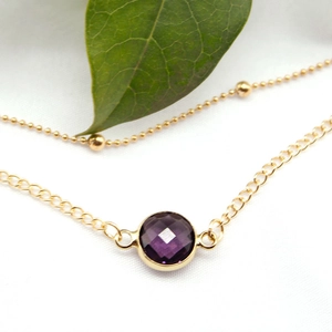 Detail of a double-layered gold alloy anklet featuring a round faceted purple gemstone