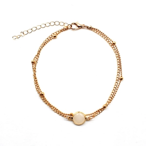 Detail of a double-layered gold anklet with round white gemstone and lobster clasp