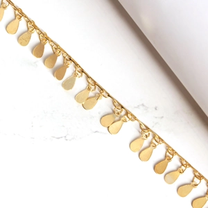 Macro shot of gold teardrop charms on a polished chain anklet over marble background