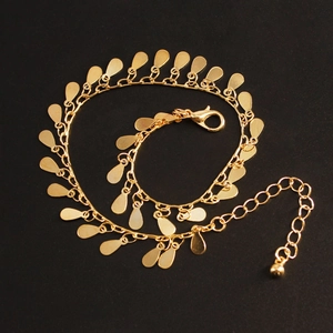 Detailed macro view of gold-plated beach anklet with reflective teardrop metal charms