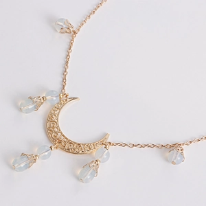 Détail du pendentif lune doré avec des pierres opalescentes et des motifs tourbillonnants