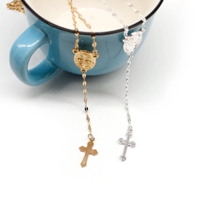 Detail of silver and gold St. Benedict cross necklaces hanging on a blue ceramic cup