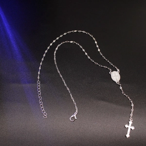 Close-up of silver cross necklace with oval medal pendant and lobster clasp detail