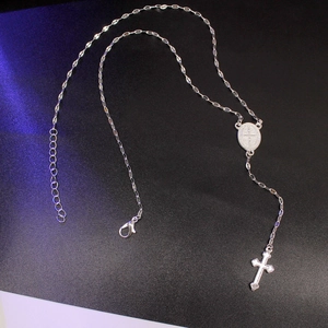 Macro detail of silver Saint Benedict medal and cross pendant on adjustable link chain