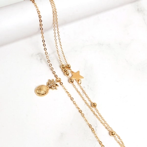 Detail of layered gold anklet featuring crystal pineapple and polished star charms