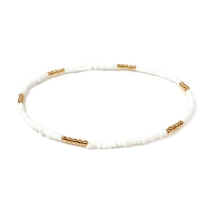 Close-up of handmade white beaded necklace with gold metal accents on plain background