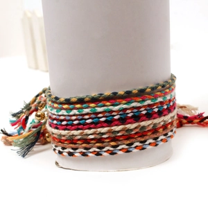 Detail of colorful hand-woven bracelets with golden bell charms on a white display pedestal