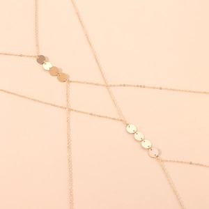 Minimalist gold body chain with shimmering round disc pendants on a soft pink background