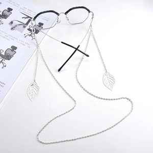 Silver metal eyewear chain with leaf pendants and black framed glasses on a magazine