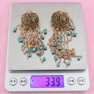 Detailed weight display of vintage gold tassel earrings with turquoise beads on a scale