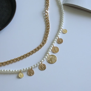 Detail of layered gold alloy curb chain and pearl body jewelry with vintage coin pendants