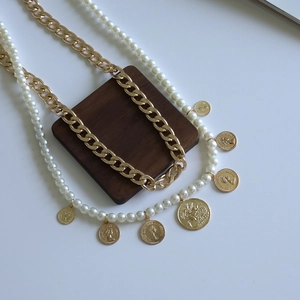 Detail of layered gold cuban chain and pearl necklace with embossed coin pendants