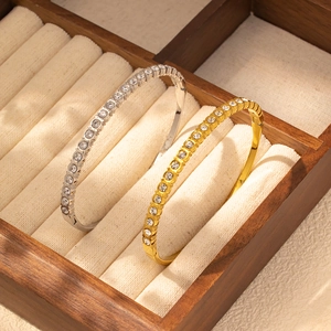 Primer plano de pulseras de acero de titanio oro y plata con circonitas en caja de madera
