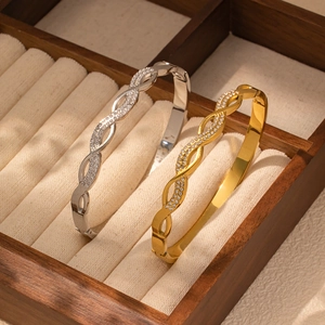 Primer plano de brazaletes trenzados de oro y plata con circonitas en joyero de madera
