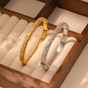 Detalle de brazaletes de acero inoxidable ondulados con circonitas en oro y plata