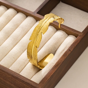 Dettaglio del bracciale a fascia piuma dorata in una lussuosa confezione regalo in legno