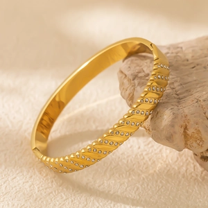 Détail d'un bracelet en acier doré avec texture irrégulière et incrustation de cristaux