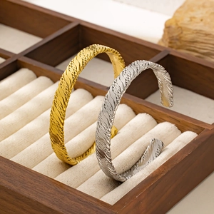 Dettaglio dei bracciali a C intrecciati oro e argento in una scatola porta gioie in legno