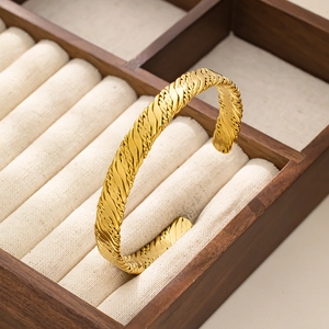 Dettaglio della texture intrecciata placcata oro su un bracciale rigido in acciaio inox
