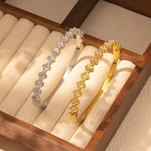 Detalle de brazaletes de trébol en oro y plata con circonitas sobre joyero de madera