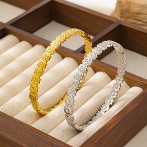 Dettaglio di bracciali in acciaio oro e argento con quadrifoglio in portagioie di legno