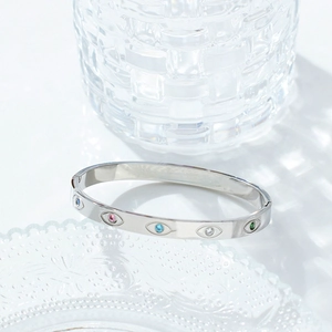Detail of silver stainless steel bangle with colorful gemstones and evil eye patterns