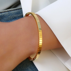 Poliertes 18k vergoldetes Edelstahl-Armband mit Struktur auf Denim-Hintergrund