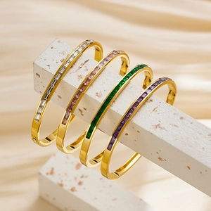 Detail of four gold-plated bangles with colorful baguette zircon stones on concrete stand