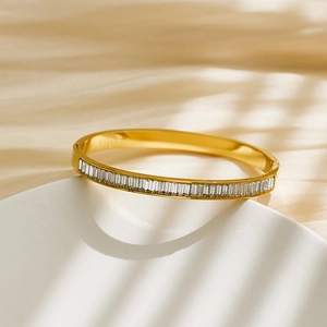 Detailed close-up of gold-plated bangle featuring rectangle-cut zircon stones on a white stand