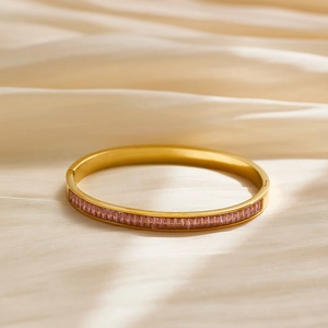 Detail view of gold titanium bangle with pink baguette-cut zircons on silk background