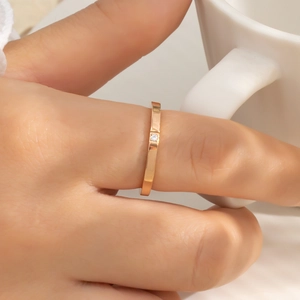 Rose gold stainless steel ring with a single zircon worn on a hand holding a white cup