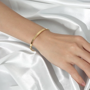 Detail of a 18k gold plated stainless steel C-shape open bangle on a white silk background
