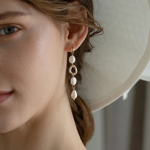 Close-up of elegant gold long drop earrings featuring three white baroque pearls on a model