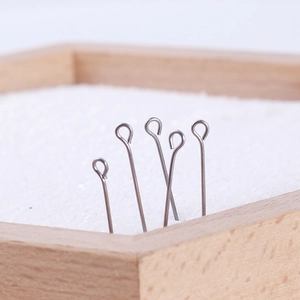 Five stainless steel eye pins for DIY jewelry making on a natural wood display background