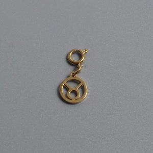 Macro shot of gold-plated Taurus zodiac pendant with spring ring clasp on gray background