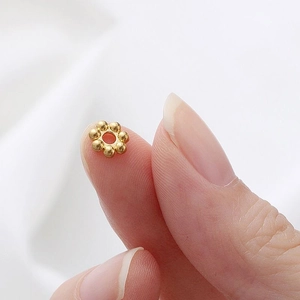 Macro di piccole perline distanziatrici a forma di fiore dorato sulla punta di un dito