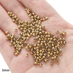 Detailed macro view showing 3mm gold stainless steel spacer beads held in hand for scale