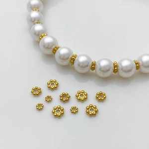 Vista macro di distanziatori dorati a fiore e collana di perle per accessori fai da te