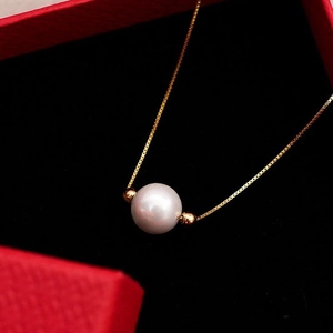 Primo piano di una collana con perla bianca e catena dorata su un portagioie in velluto rosso