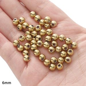 Detailed macro view of 6mm polished gold stainless steel beads held in hand for DIY jewelry