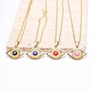 Gold evil eye pendant necklaces in four enamel colors on a textured stone surface
