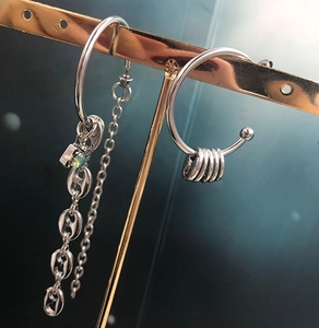 Macro view of silver stainless steel asymmetric earrings with chain links and green stone